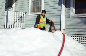 Petro delivery driver surrounded by snow with a hose attached to the home's cleared fill pipe